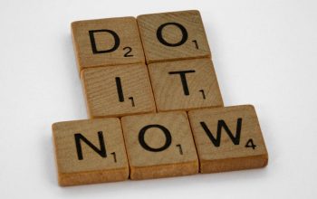 Wooden scrabble tiles forming 'DO IT NOW' on a minimal white backdrop. Inspiring concept.