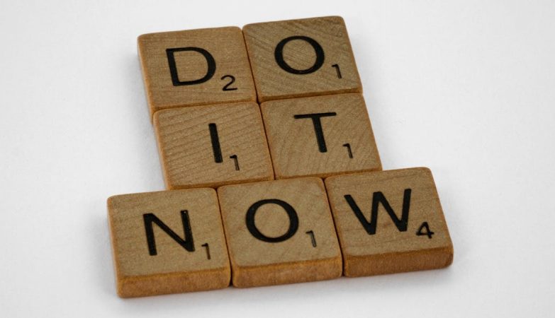 Wooden scrabble tiles forming 'DO IT NOW' on a minimal white backdrop. Inspiring concept.